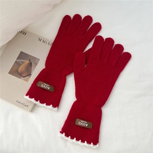 Close-up of red knit gloves featuring white scalloped edges and leather handmade label