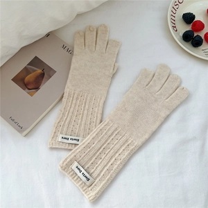 Detail of cream knit gloves featuring fingerless design and branded woven label