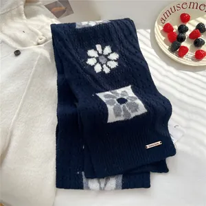 Detail of navy knit scarf with floral patterns and branded metal tag on cozy background