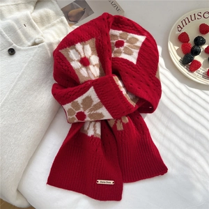 Detail of red floral knit scarf with gold brand tag on soft white bedding background