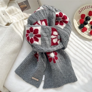 Detail of grey knitted wool scarf featuring large red floral patterns and metal brand plate