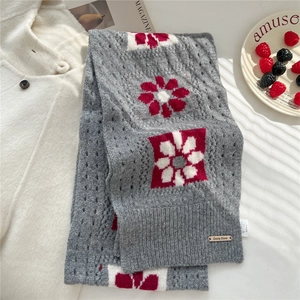 Close-up of grey knitted wool scarf featuring red floral patterns and metal brand plaque