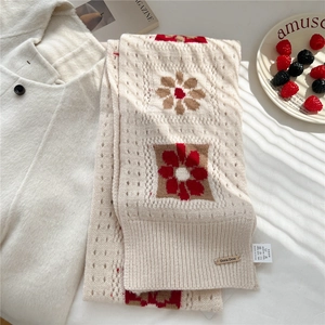 Detailed close-up of cream knitted wool scarf featuring floral patterns and metal brand tag