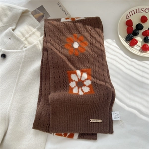 Detail of soft brown knit wool scarf featuring large orange floral patterns and metal tag