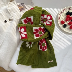 Close-up of thick green knit scarf featuring red floral patterns and metal brand tag