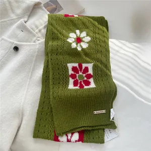 Close-up of green floral knit wool scarf showing flower patterns and metal brand logo