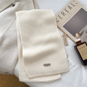 Detail of cream knit wool scarf featuring a leather logo patch and textured weave