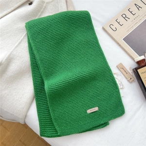Macro detail of green chunky knit wool scarf texture with brand tag on soft white fabric