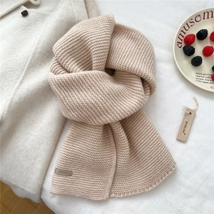 Detailed close-up of chunky knit beige wool scarf with a leather brand tag and wood label