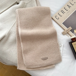 Close-up of beige knitted wool scarf with premium leather brand logo label detail