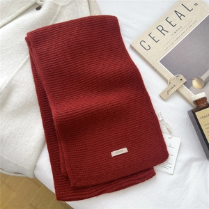 Close-up of deep red knitted wool scarf with textured vertical patterns and brand tag