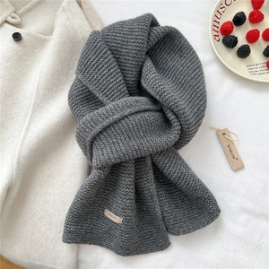 Detail of grey knitted wool scarf featuring brand label and textured rib stitch pattern