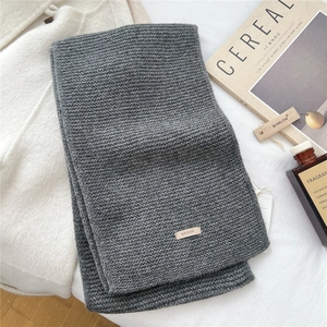 Detail showing deep grey knitted wool scarf texture with brand logo and warm winter styling