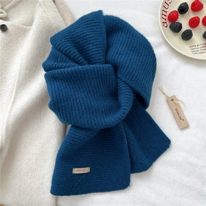 Detail of navy blue knit wool scarf with brand label and winter-themed lifestyle setup