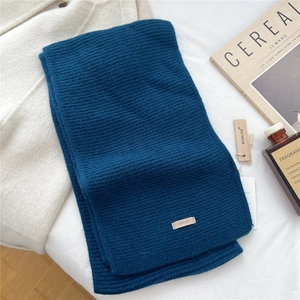 Macro view of peacock blue waffle knit wool scarf with premium leather brand tag