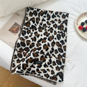 Detail shot of leopard print wool blend scarf with BOWLOW label on a soft bed