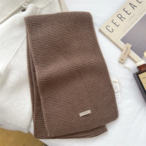 Close-up of brown chunky knit wool scarf texture with branding label and wood tag