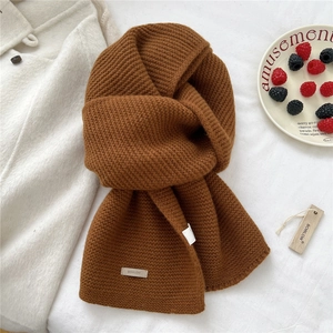Close-up of caramel thick knit wool scarf with leather brand label on white fabric