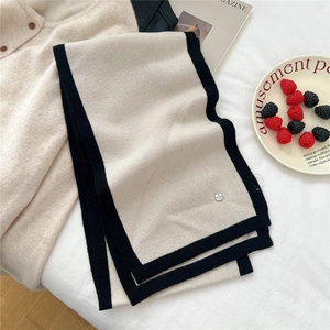 Close-up of beige knitted wool scarf with black border and round metal logo detail