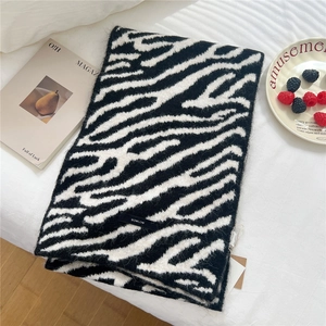 Detailed macro shot of zebra print wool blend scarf texture with brand tag on soft bedding