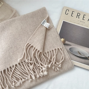 Close-up of beige knitted scarf with 100% wool label and handmade tassel details