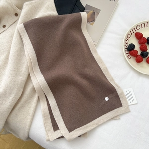Detailed knit texture of a dual-color wool scarf with a silver logo tag and premium tag