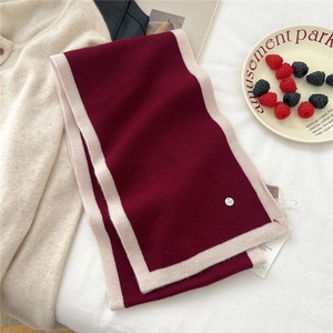 Detail of burgundy knitted scarf with pink contrast trim and metallic brand logo