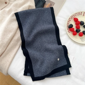Close-up of charcoal grey wool knit scarf featuring black contrast edges and silver metal tag