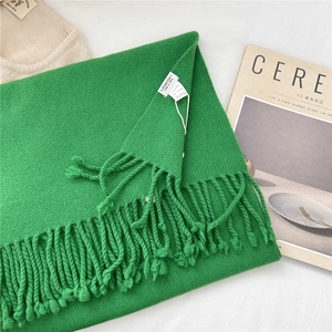 Detail of green knitted wool scarf featuring neat fringe and a 100% wool label