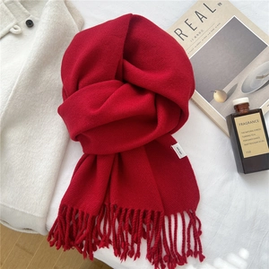 Close-up of red 100% wool scarf with fringe detail on a soft white fabric background