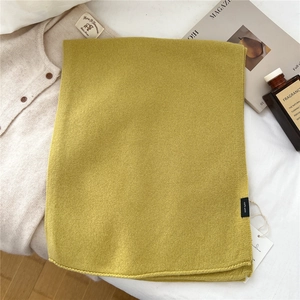Detail of lime green 100% wool scarf featuring fine knit texture on white bedding