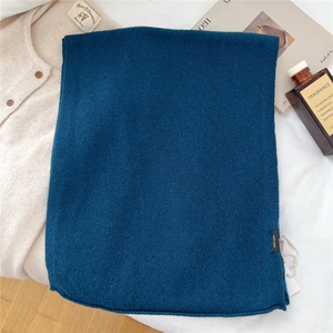 Detail of dark teal 100% wool scarf featuring a woven label and premium knit texture