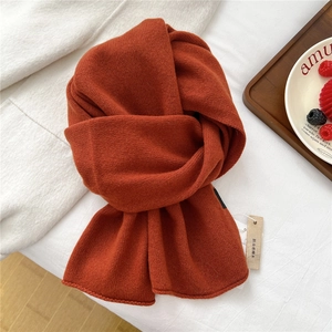Detail of orange knit wool scarf with protective camphor wood tag on soft white blanket