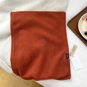 Detailed view of the 100% wool knit scarf texture in burnt orange with quality labels