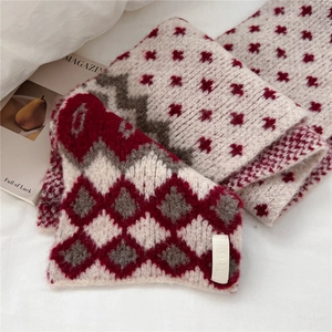 Detailed view of jacquard geometric patterns on a soft cream knit scarf with red and grey