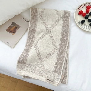 Detail of soft diamond pattern knit scarf with stitched label on cozy bedding