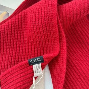 Detail of red wool scarf featuring thick rib knit texture and material tag for women