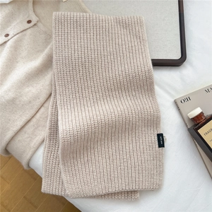 Detailed close-up of beige knit wool scarf texture with 100 percent wool label