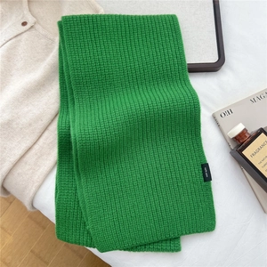 Detail shot of the 100% wool material label on a vibrant green thick ribbed knit scarf
