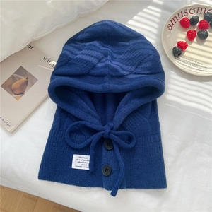 Detail of navy knit balaclava with buttons and label on white bedding with soft shadows