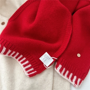 Detail of red wool scarf featuring 100% wool label and white striped knit texture