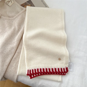 Detail of knitted wool scarf featuring beige texture with red rib trim and round letter D buckle