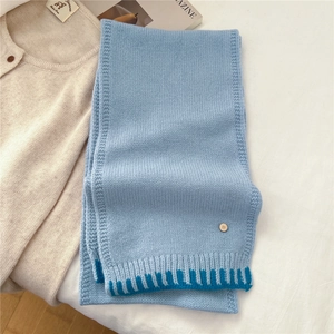 Detailed knit texture of light blue wool scarf with dark blue stripes and metal charm