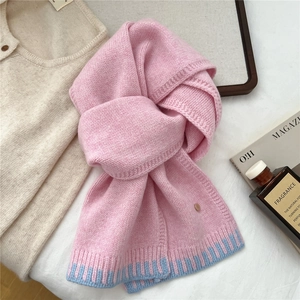 Detail of pink knitted wool scarf with light blue striped ends and decorative metal plate