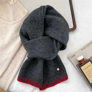 Detailed knit texture of dark grey wool scarf with red stripes and metal logo