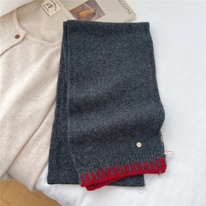 Detail of dark grey knit wool scarf with red contrast edges and a gold 'D' metal logo