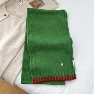 Close-up of green wool scarf texture with red stripes and round metal logo detail