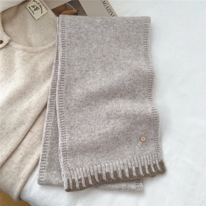 Detail of oatmeal knit wool scarf with dark brown ribbed hem and metallic logo