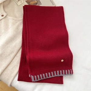 Detail shot of a red knitted wool scarf featuring a metallic logo tag and striped hem