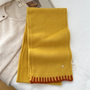 Detailed knit texture of ginger wool scarf with red zigzag edge and metal charm